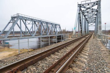 Nehir üzerinde demiryolu rayları olan iki paralel metal köprü. Riga, Letonya 'nın ilkbahar manzarası.