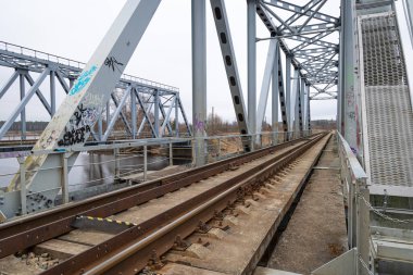 Nehir üzerinde demiryolu rayları olan iki paralel metal köprü. Riga, Letonya 'nın ilkbahar manzarası.