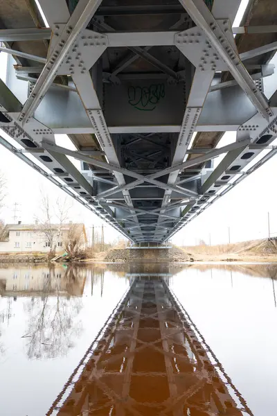 stock image A beautiful springtime scene under the old metal railway bridge over the river. Metal construction from below.