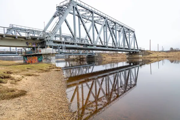 Bulutlu bahar gününde nehrin üzerindeki metal bir köprü. Riga, Letonya 'da doğal ilkbahar manzarası.