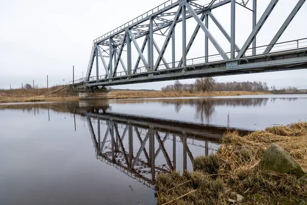 stock image A metal truss bridge over the river in overcast spring day. Natural springtime scenery in Riga, Latvia.