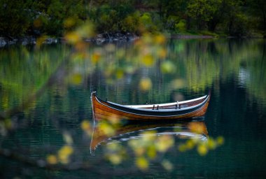 Kuzey Norveç 'teki dağlarda sonbahar gölünde yüzen güzel bir tekne. İskandinavya 'nın mevsimlik manzarası.