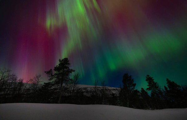 A beautigul autora borealis display over the snowy Norvegian winter landscape. Northern lights in Norway sky. Arctic nature in Scandinavia during winter season.