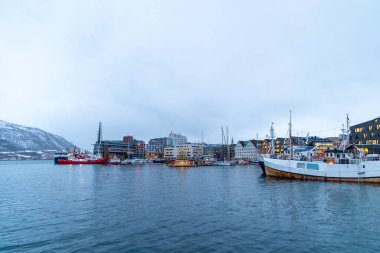 Bulutlu bir kış gününde güzel bir Tromso limanı manzarası. Gemiler ve şehir binaları. Kış mevsiminde İskandinavya 'da Kuzey Kutbu doğası.