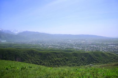 Tepeleri ve yeşil tepeleri olan bir dağ vadisinin uzak manzarasında vadide, baharda, güneşli bir köy bulunur.