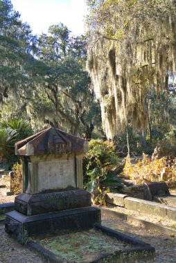 Huge stone statue in historic Bonaventure Cemetery with spanish moss hanging from live oaks over the grave sites in the early morning sunlight.
