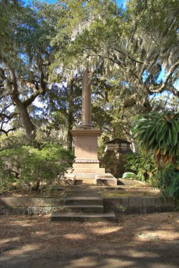Huge stone statue in historic Bonaventure Cemetery with spanish moss hanging from live oaks over the grave sites in the early morning sunlight