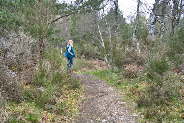 Woman wearing a vest on a tree lined hiking trail in early spring rural Scotland.