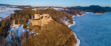 Polonya, Czorsztyn 'deki ortaçağ şatosunun kalıntıları. Kışın gün batımında, Dunajec Nehri 'nde donmuş yapay Czorsztyn Gölü ile birlikte hava manzarası. Arka planda Czorsztyn köyü.