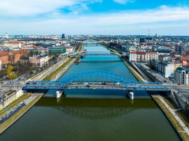 Polonya, Krakow 'daki Vistula Nehri' ndeki köprüler. Hava görüntüsü. Uyanık insanlarla bulvarlar. Önde mavi kemerli köprü. Yayalar ve bisikletçiler için yaya köprüsü. Çifte demiryolu köprüsünün uzak görüşü