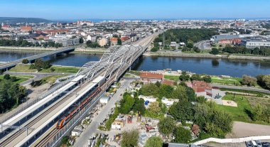Hızlı şehir treni, yeni Krakow Zablocie tren istasyonu ve yeni üçlü kemerli demiryolu köprüsü dört raylı, yaya köprüsü ve Polonya 'nın Krakow kentindeki Vistula nehri üzerinde bisiklet yolu. Hava görünümü