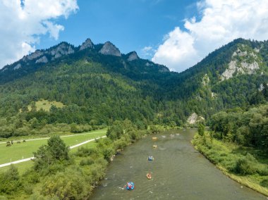 Polonya 'daki Pieniny Dağları' ndaki Dunajec Nehri Boğazı 'na yaklaşan ahşap veya pnömatik sallar ve kanolardaki turistler. Trzy Korony (Üç Karga) Pieniny 'nin arka plandaki en yüksek zirvesi 
