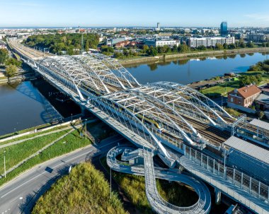 Polonya 'nın Krakow kentindeki Vistula nehri üzerinden yeni Krakow Zablocie tren istasyonuna giren dört raylı, yaya köprüsü ve bisiklet yolu olan yeni üçlü köprü üzerindeki hızlı şehir treni. Hava görünümü