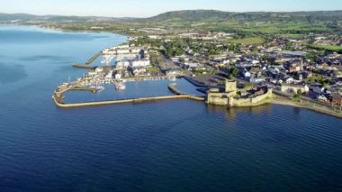 Belfast Lough, Carrickfergus 'taki Ortaçağ Norman Kalesi' nde gün doğumunda Belfast yakınlarında. Marina, breakwater, yatlar, park alanı, kasaba ve arka planda Belfast manzaralı 4K video 'ya yaklaşıyor.. 