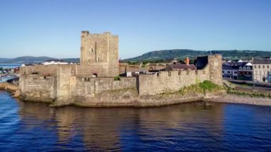 Belfast Lough, Carrickfergus 'taki Ortaçağ Norman Kalesi' nde gün doğumunda Belfast yakınlarında. Marina, breakwater, yat, park yeri, kasaba ve arka planda Belfast manzaralı 4K pansiyon videosu.             