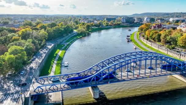 在波兰克拉科夫的维斯瓦河上的毕苏斯基蓝色系弧桥上 两辆电车相互来往 河岸上的城墙 林荫大道和长廊上挤满了行人和骑自行车的人 Aerial Video — 图库视频影像