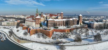 Krakow, Polonya. Kraliyet Wawel Katedrali ve kalesi kışın karla kaplıdır. Vistula Nehri ve turist tekneleri. Bulvar, gezinti yerleri ve yürüyen insanlarla dolu bir panorama. Arka planda eski şehir