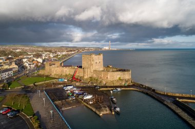 Ortaçağ Norman Kalesi, Carrickfergus 'ta tekne rampası ve dalga kırıcısı olan liman Belfast, Kuzey İrlanda, İngiltere yakınlarında. Kışın gün batımında hava manzarası. Kasaba ve fırtınalı bulutlar arka planda