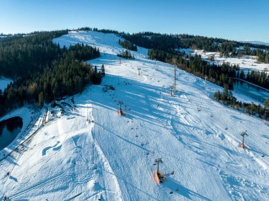 Kışın Polonya 'nın Kotelnica Dağı' ndaki Bialka Tatrzanska kayak merkezinde kayak pisti, teleferikler, kayakçılar ve snowboardcular. Düşük Aralık ışığı altında hava görüntüsü