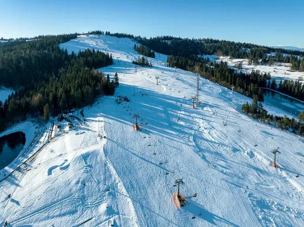 スキー場 チェアリフト スキーヤー スノーボード 冬のコテルニカマウンテンでポーランドのビオカルタトルツァスキーリゾート 低い12月のライトの空中眺め ストック写真