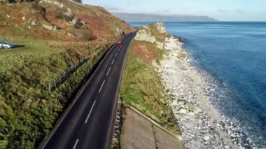 Kuzey İrlanda, İngiltere, kayalıkları olan Atlantik kıyıları. Antrim Coast Yolu 'ndaki kırmızı araba. Nam-ı diğer... Causeway Sahil Yolu. Avrupa 'nın en manzaralı kıyı yollarından biri. Hava 4K videosu. Kış, gün doğumu