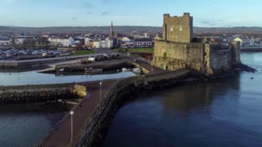 Ortaçağ Norman Kalesi ve Carrickfergus Limanı. Gün batımında Belfast yakınlarında. Hava 4K uçuş videosu su yansıması, marina, tekne rampası, dalgakıran ve kasaba 