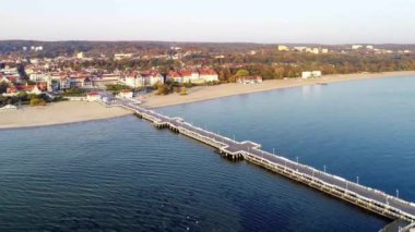 Polonya 'da ahşap iskelesi, marinası, yatları ve kumlu plajı olan Sopot tatil köyü. Hava 4K gündoğumu ışıklarındaki videoyu gösteriyor / uçuruyor