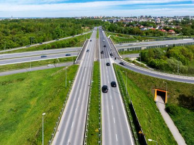 Polonya, Krakow 'da A4 otoyolu ile çok katlı şehir otoyolu kavşağı. Arabalar, trafik, rampalar, yeraltı patikaları ve bisiklet yolları. Hava görüntüsü. Arka planda şehir