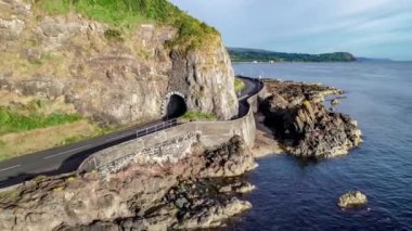Kara Yay tüneli olan Causeway Sahil Yolu. Antrim County, Kuzey İrlanda 'nın doğu kıyısı boyunca giden manzara yolu. Hava 4k gündoğumu ışıklarındaki videoyu gösteriyor