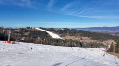 Polonya 'nın Podhale bölgesindeki Bialka Tatrzanska kayak merkezinde kayak pistleri, yapay kar, teleferikler, tanınmayan kayakçılar ve snowboardcular. Mavi gökyüzünde kopyalama alanı olan 4K video