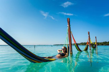 Beautiful white female tourist relaxing in a hammock in Laguna Bacalar in Mexico during kayak trip.