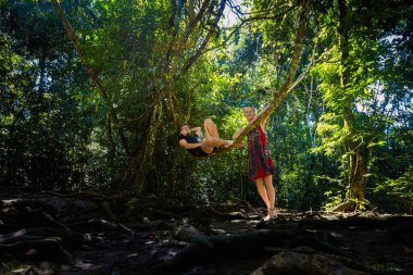 Young pretty couple man and woman in Roberto Barrios cascadas park, sitting on a tree, Palenque in Mexico. Vivid landscape photo with lush green during sunny day. clipart