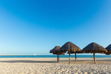 Güneşli bir günde Meksika 'daki güzel Progreso plajı. Beyaz sahilde doğal şemsiyeler ve mavi gökyüzü.