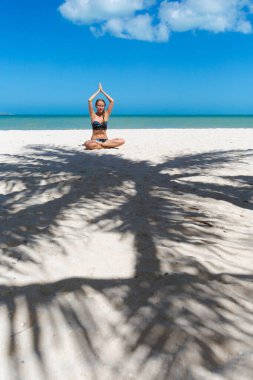 Güneşli bir günde Progreso sahilinde meditasyon yapan güzel bir genç kadın. Palmiyeleri ve mavi gökyüzü olan beyaz sahil.