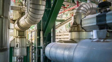 Sarı şeritli bir boru kırmızı şeritli bir boruya bağlıdır. Borular büyük bir endüstriyel binaya bağlı.