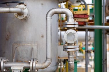 Bir kimya fabrikasındaki borulara yerleştirilen yan cam pencere, sıvı akışının ve içerideki koşulların gözlemlenmesine olanak sağlayarak güvenlik, izleme ve endüstriyel süreç kontrolünü sembolize ediyor..