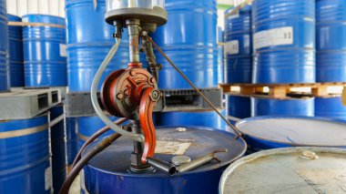 Bir deponun içindeki 200 litrelik bir petrol variline bağlı elle işletilen pompa endüstriyel ekipmanları, sıvı transferini, güvenliği ve güvenilir madde kullanımını temsil ediyor..