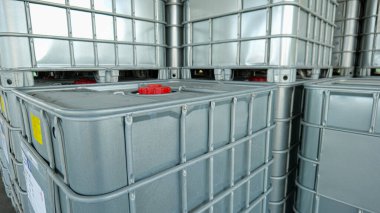 Koruyucu bir metal ızgarası tarafından korunan plastik kübik kimyasal sıvı konteynır depolama, depolama ve endüstriyel tedarik konseptini temsil eden bir depo fabrikası ortamında saklanıyor..