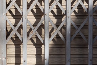 Izgara metal kapı, doğal ışığın oluşturduğu soyut gölgelerle korunarak tasarım, inşaat ve mimari projeler için ideal çok yönlü endüstriyel bir arka plan oluşturur..