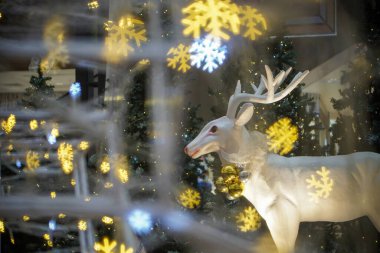 Kar tanesi ön planında beyaz geyik heykeli. Noel, kış tatili teması