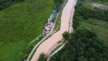 Nehrin yanındaki yeşil yemyeşil yemyeşil çimenlikte yanan çöpleri yakan drone atışı.