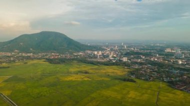 Aerial hyperlapse move over green paddy field toward Bukit Mertajam town in evening