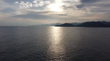 Gün batımında arka planda görkemli dağlarla çevrili sakin deniz.