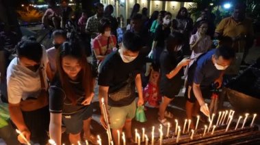 Bukit Mertajam, Penang, Malezya - 28 Haziran 2023: Yavaş çekim mum alevleri coşkulu dindarların yüzlerini aydınlatarak, Aziz Anne 'in yıllık ziyafeti sırasında sarsılmaz inançlarını ifade eder.