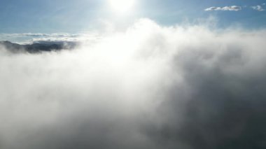 Yükseltilmiş bakış açısı, alçak bulutlar ve uzak tepelerle dolu bir sabah sahnesinin huzurlu atmosferini vurguluyor.