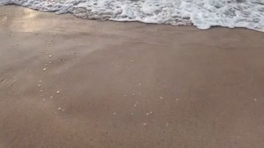 Okyanus sakin ve su beyaz. Kum kahverengidir ve dalgalar küçüktür