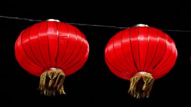 Bir telden sarkan iki kırmızı fener. Biri diğerinden daha aşağıda duruyor. Alttaki fener yere daha yakın duruyor.