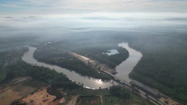Resimde ortasında bir köprü bulunan bir nehir gösteriliyor. Köprü ağaçlar ve binalarla çevrilidir. Hava görüntüsü Kota Tinggi, Johor