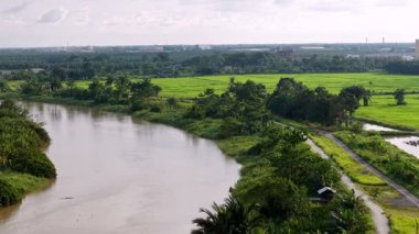 Nehrin diğer tarafında yeşil bir alan var. Su kahverengi ve gökyüzü bulutlu.