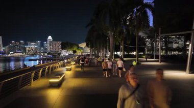 Marina Bay, Singapore - Jul 09 2024: A group of people walking on a sidewalk. There are some benches along the sidewalk